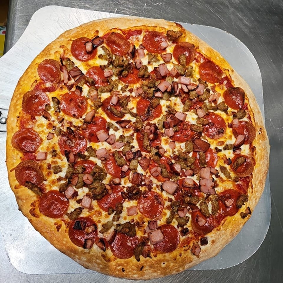 A Big's Pizza and Subs meat lover's pizza, topped with pepperoni, sausage, and ham, on a metal peel.