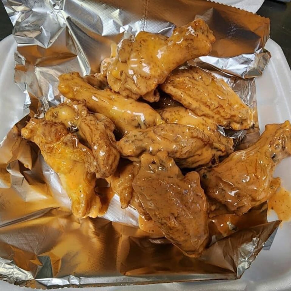 Big's Pizza and Subs' chicken wings, coated in a rich, creamy sauce, served in a foil-lined container.