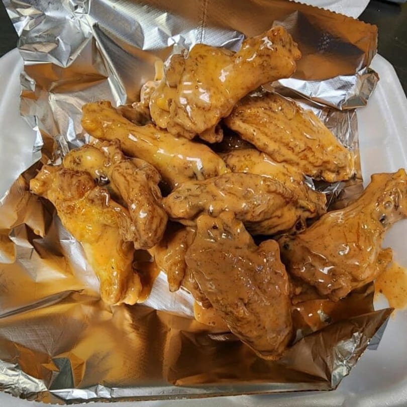 Big's Pizza and Subs' chicken wings, coated in a rich, creamy sauce, served in a foil-lined container.