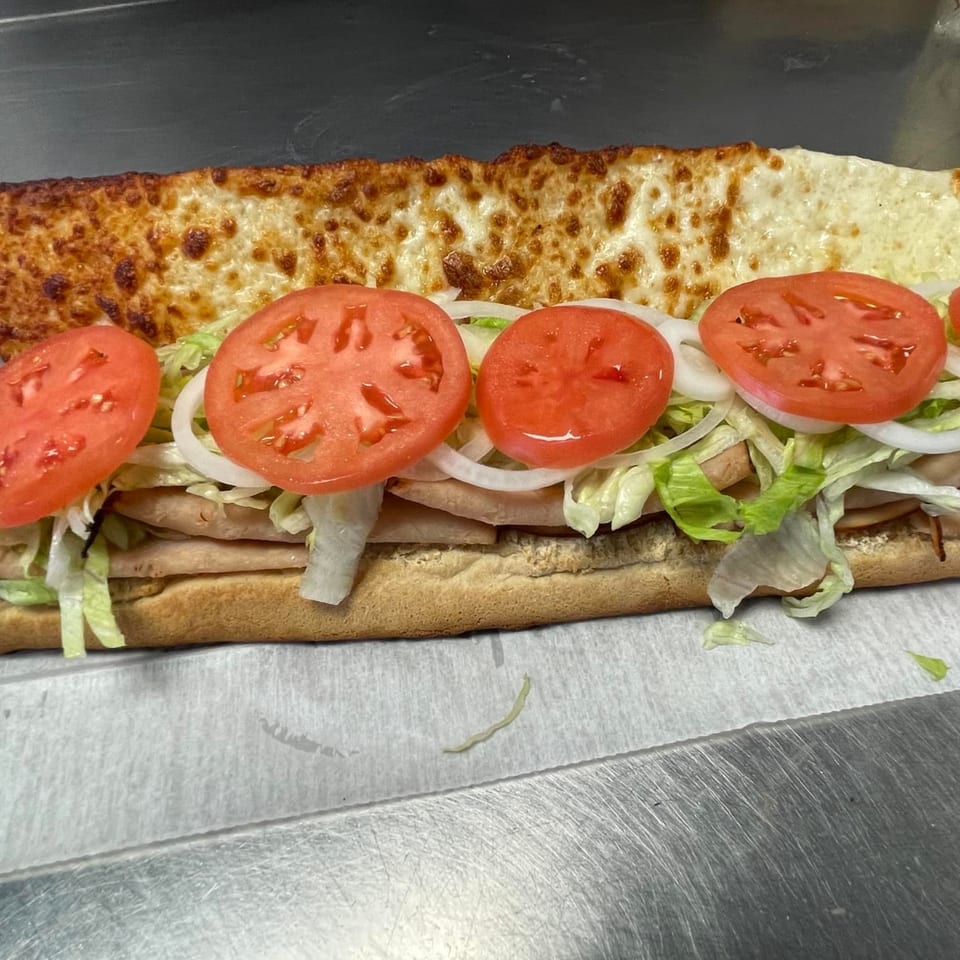A toasted Big's Pizza and Subs sub sandwich with melted cheese, turkey, lettuce, onions, and tomatoes.